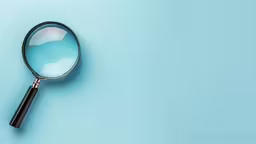 a magnifying glass sitting on top of blue paper,a magnifying glass lies next to the top of a blue background