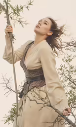 a woman in a long dress holding up branches