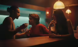 three people sitting at a bar looking at each other
