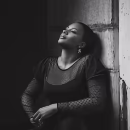 black and white photograph of woman leaning up against the wall