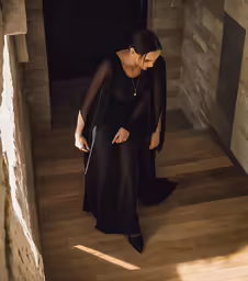 woman in black sheer dress with cape over shoulder standing on wood floor