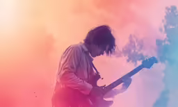 a young man holding his electric guitar while standing in front of an orange and pink background