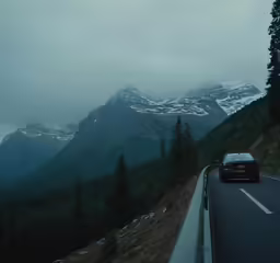 cars drive down a road near snow covered mountains