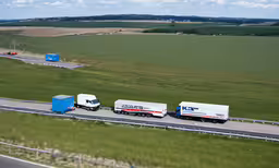 a group of semi trucks traveling down a road,three semi - trucks traveling on a highway with an overpass behind them