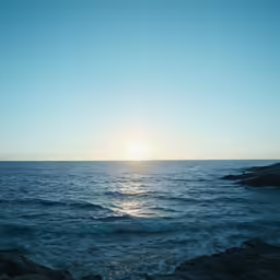 the sun shines brightly over the ocean and rocks