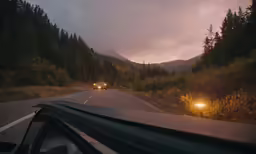 the view of two cars driving down a road near mountains