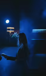 a woman in a dimly lit room and a plant