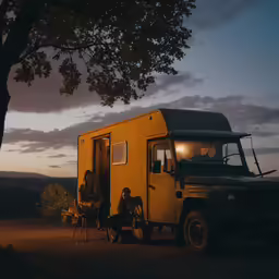 two people sit in the doorway of a tiny, yellow truck