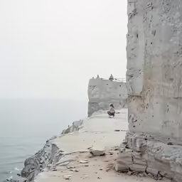 a person sits on a rocky cliff with sea in the background