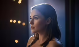 a woman looking to the side while standing in front of a window