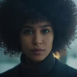 woman with dark hair and black turtleneck stares at camera