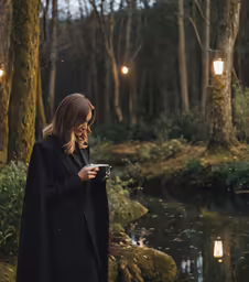 a woman in a black coat and jacket standing by a creek