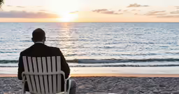 a man sitting on a beach in a white chair looking at the ocean