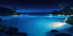 a beautiful pool with lights next to rocks and grass
