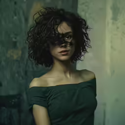 woman with dark curly hair and green off shoulder top looking into camera