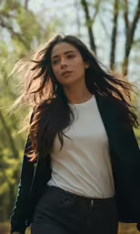 a woman with long hair walking through the woods