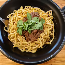 a black bowl filled with pasta and beef