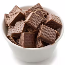 a bowl full of chocolate squares sitting in front of white background
