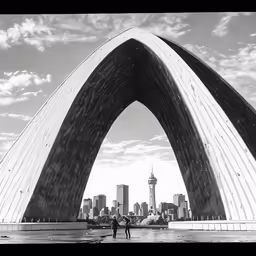 two people are standing on a pier near a giant arch