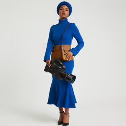 a woman posing in a blue dress, and holding a camera