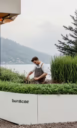 a man kneeling in a garden with tall plants and grass around him