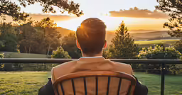man sitting in chair with sun setting behind him
