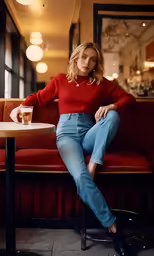 a woman in a red sweater and jeans sitting on a bench