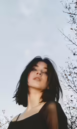 a young lady with dark hair poses near tree branches