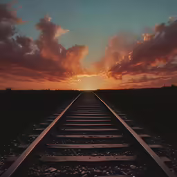 a train track running under a sunset with the sun going down