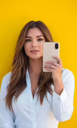 young woman taking selfie using cell phone against yellow wall