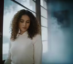 a woman with long brown curly hair looking out the window