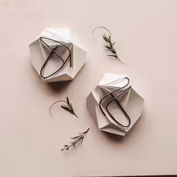 two origami vases are on a table with olive twigs