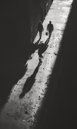 people walking down a sidewalk next to the shadows of buildings