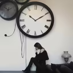 a woman sits on the floor beside two large clocks