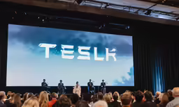three people standing in front of a large screen with a man standing on a stage speaking