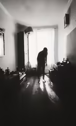 the black and white image shows the silhouette of someone standing in a room with bright light shining in