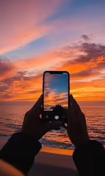 a person holding up an iphone taking pictures of the sunset