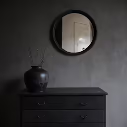 a black dresser with vase and mirror on it