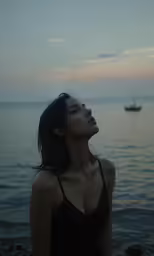 a woman is standing by the ocean watching something in the sky