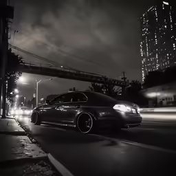 a dark colored car driving on a road in the city at night