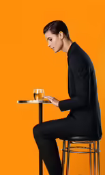 a woman in black sitting at a table with a glass of wine