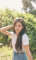 a girl in a white shirt and blue denim overalls standing by bushes