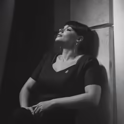 a woman is leaning up against a wall and looking up