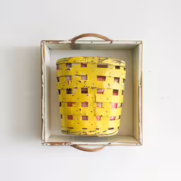 a basket that is sitting in an old box,a yellow basket with a handle is in a white case
