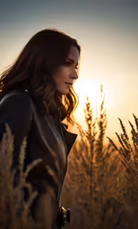 a woman is standing in the grass at sunset