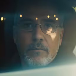a man wearing glasses and standing in front of a mirror