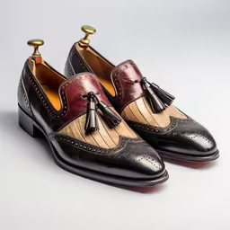 two tone leather tasseled shoes on white surface,a pair of black and maroon shoes with two tone tassels