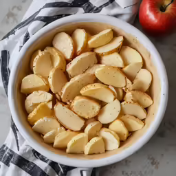 a bowl full of sliced potatoes next to an apple