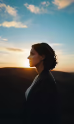 a person with hair blowing back standing with the sun setting behind them