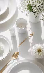 a white table set for two with flowers and plates